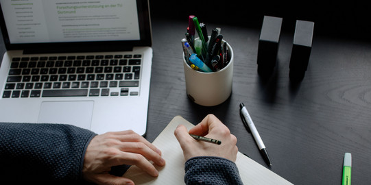 A student working at a table with a laptop, pencils and a notebook.